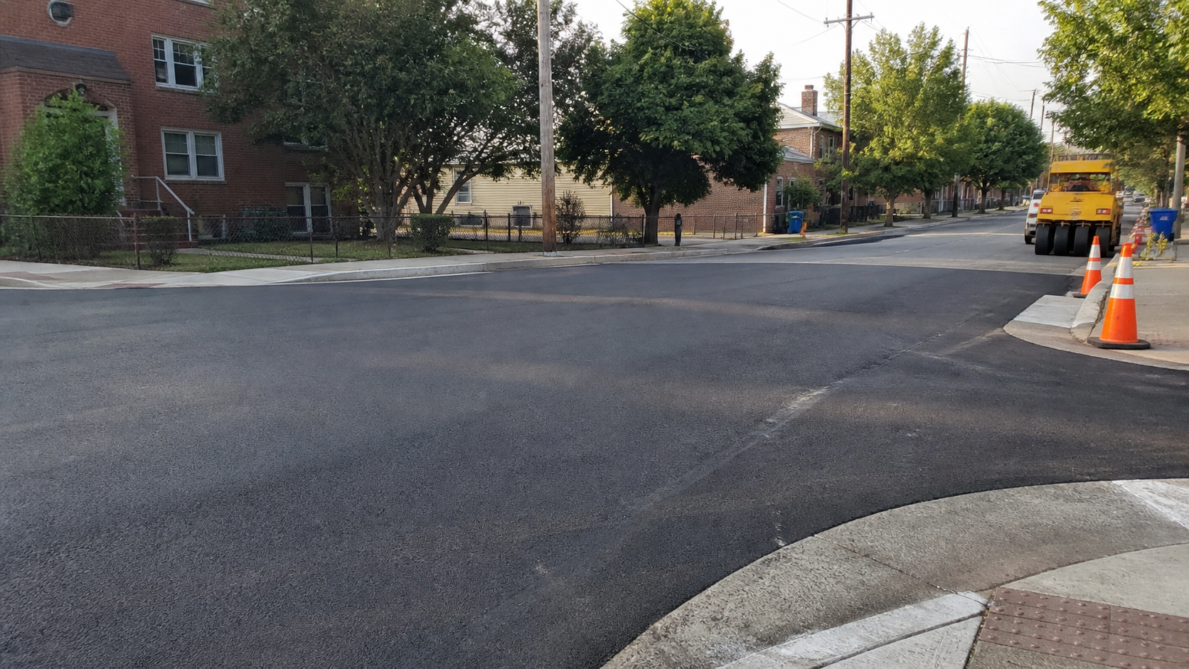 Freshly paved Greensboro neighborhood intersection with traffic cones and roadwork equipment
